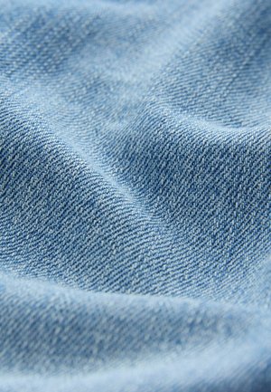 Hellblaues Denim-Gewebe mit einer glatten Textur und einem dezenten Webmuster. Die Oberfläche zeigt sanfte Falten und natürliche Knicke.