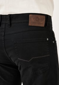 Schwarze Denim-Hosen mit einem Lederpatch auf der Rückseite, auf dem "redpoint" steht. Enthält doppelte Nähte an den Gesäßtaschen und Metallknopfdetails.