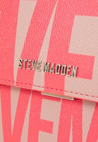 Nærbillede af struktureret pink og beige læder med sølvmetal "Steve Madden" branding på en syet klap.