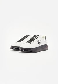 White sneakers with black laces and a dark translucent sole. Features a graphic of a character in sunglasses on the outer side.