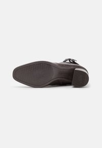 Zapato de cuero negro con suela texturizada y tacón bajo, detalle de hebilla en la parte superior, marcaje de suela antideslizante, colocado de lado sobre un fondo blanco.