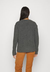 Svetr z úpletu v barvě uhelně šedé s kulatým výstřihem, žebrovaným lemem a spadlými rameny, spárovaný s kalhotami z tkaniny manšestr v béžové barvě.