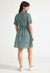 Grøn blomsterkjole med korte ærmer, krave, indsnævret talje og en udvidet nederdel. Stylet med hvide sneakers for et afslappet look.