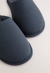 Páros tengerészkék, texturált benti papucs világos háttéren, részletes közeli felvétel a szövet és a varrás részleteiről.