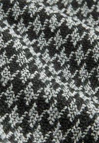 Mustvalge kootud kangas, millel on houndstooth muster. Tekstuuriga pind, mis sisaldab erinevaid kiude, luues pehme väljanägemise.
