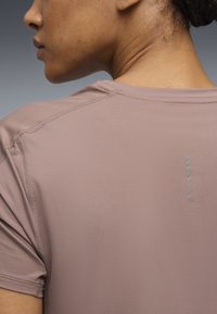 Άτομο που φοράει φωτεινό μωβ κοντομάνικο πουκάμισο με ανάγλυφη υφή και μικρό κάθετο ανακλαστικό λογότυπο στο πάνω μέρος της πλάτης.