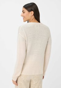Cremefarbener Strickpullover mit langen Ärmeln, rundem Ausschnitt und einer weichen, strukturierten Oberfläche. Der Rücken weist eine nahtlose Verarbeitung auf.