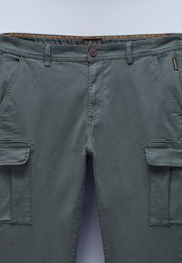 Dark gray cargo pants made of soft fabric. Features two side pockets, a button closure, and a stitched waistband with a patterned trim.