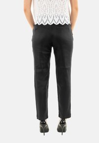 Pantalones ajustados negros con una textura suave y un corte slim, que cuentan con dos bolsillos traseros y se combinan con zapatos de tacón alto negros. Parte superior de encaje blanco visible.