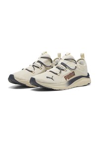Zapatillas deportivas color crema con una parte superior de malla texturizada, cordones oscuros y un logo de Puma naranja en el lateral. Con una suela de goma texturizada.