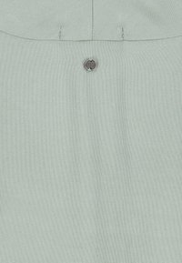 Light green fabric with a small round metal button inscribed with "SELVA CENTREF" near top center and stitched seams above.
