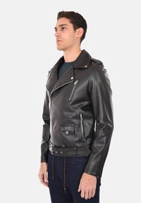 Giacca da motociclista in pelle nera con tasche con zip, revers ampi e vita con cintura. La texture liscia e il design aderente mettono in risalto la sua forma.
