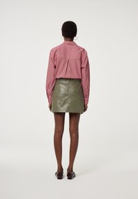 Rode en witte gestreepte blouse met een losse pasvorm en plooien aan de achterkant, gecombineerd met een groene leren minirok en glanzende burgundy schoenen.