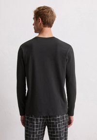 Zwarte longsleeve shirt van zacht materiaal, met een ronde halslijn en een relaxte pasvorm, gedragen met grijze geblokte broek met een patroon.