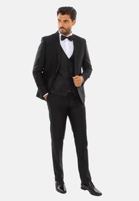 Abito nero con rever in satin, camicia bianca e papillon. Gilet a trama, pantaloni aderenti e scarpe eleganti nere lucide.