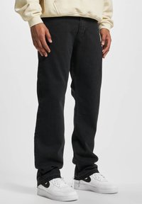 Black denim jeans with a relaxed fit, featuring a straight leg silhouette. Worn with white sneakers, showcasing a casual outfit.