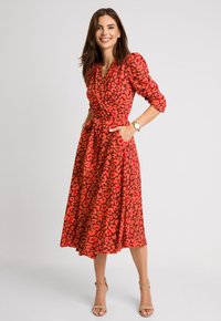 Czerwona sukienka w czarne nadruki zebry, zapinana na krzyż, z krótkimi bufkami, kieszeniami po bokach i związanym w talii paskiem. Sięga do połowy łydki.