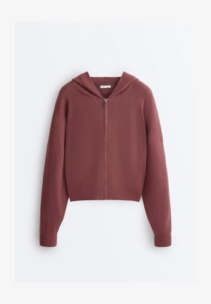 Praškasta rožnata kapucar iz rebrastega pletenega materiala z dolgim sprednjim zadrgo in dolgimi rokavi, položen na ravno belo podlago.