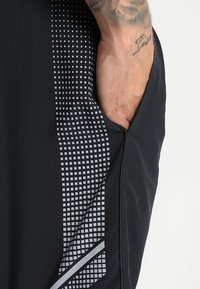 Svarta idrottsshorts med ett texturerat, geometriskt mönster i grått på sidan, med en diskret ficka och slät tygfinish.