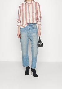 Randig button-down skjorta i vitt, orange och blått; ljusblå raka jeans; svarta ankelboots; svart handväska.