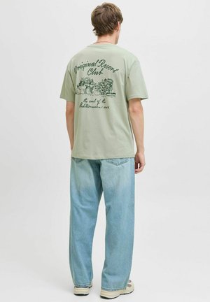Mint green t-shirt with a graphic print on the back, short sleeves, and a relaxed fit, paired with light blue wide-leg jeans.
