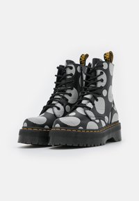 Botas de combate negras con un llamativo patrón de lunares blancos y acentos a rayas, con una suela gruesa y cordones negros. Etiqueta dorada en la parte trasera.