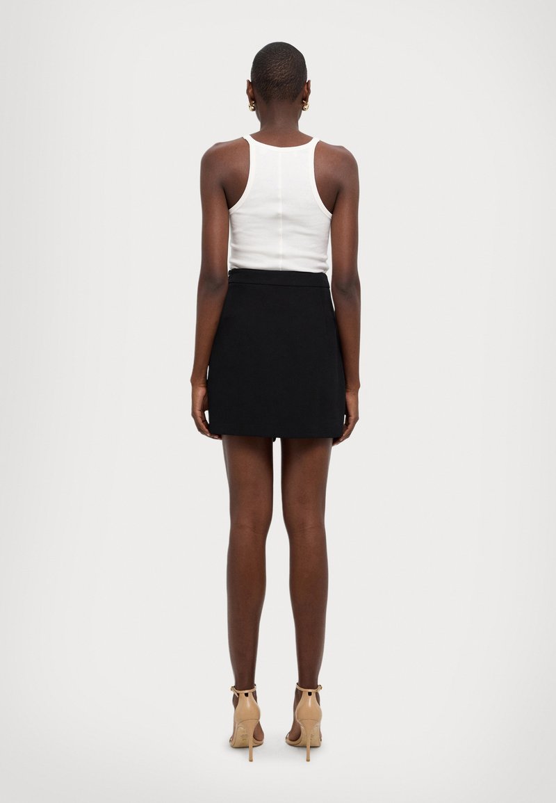 Biała bezrękawnikowa bluzka w zestawieniu z czarną mini spódnicą. Stylizacja ma dopasowany krój, gładką teksturę i beżowe szpilki.