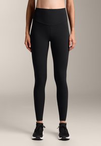 Magas derekú fekete leggings, rugalmas anyagból készültek, sima felülettel és testhezálló kialakítással, amely a lábakhoz simul.