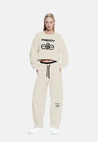 Felpa cropped color crema e pantaloni abbinati, con la scritta "FREDDY elite" in nero. Tessuto morbido con una vestibilità rilassata.