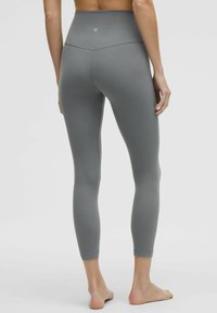 Sive visokotalasne tajice s glatkom teksturom, prilagođenim dizajnom i krojem do gležnjeva. Sadrže suptilan logo na stražnjem dijelu struka.