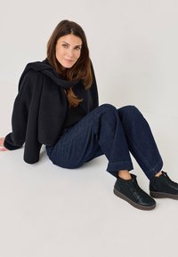 Suéter negro cortado superpuesto sobre una blusa negra, combinado con pantalones de mezclilla azul sueltos y zapatillas altas negras sobre un fondo claro.