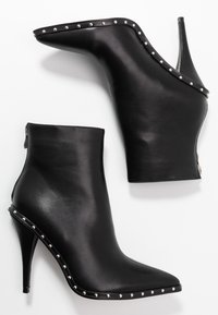 Musta nahkasaappaat nilkkapituisilla, teräväkärkisillä ja korkealla stiletto-korkealla, joissa on hopeisia niittejä reunoilla. Varustettu sivuvetoketjulla sulkemista varten.