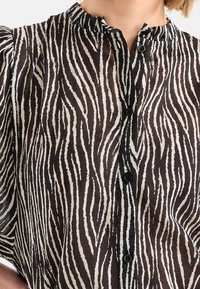 Černo-bílá košile s potiskem zebřích pruhů, lehká tkanina, zapínání na knoflík a detail s volánkem na výstřihu.