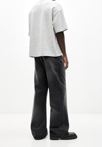 Camiseta gris de manga corta con corte relajado, combinada con pantalones vaqueros de pierna ancha gris oscuro. El conjunto presenta un diseño minimalista y comodidad casual.