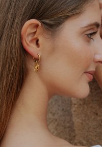 Arany karika fülbevalók napkitörés medállal. A medál sugárzó sugarakat ábrázol kifinomult mintával és fényes felülettel.