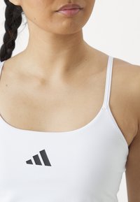 Witte sport tanktop met dunne bandjes en een zwart Adidas-logo op de borst. Glad textuur met een getailleerd ontwerp.