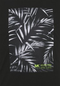 Tela negra con patrón de hojas de palma tropicales blancas y texto pequeño en amarillo-verde "MK Michael Kors" y detalles del producto en la esquina inferior derecha.