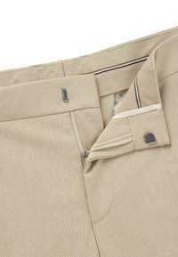 Beige trousers with a textured fabric, featuring a metal zipper, a button closure, and a classic waist with subtle striping on the waistband.