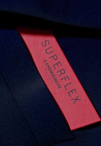 Granatowy materiał o gładkiej fakturze, z czerwoną metką, na której widnieje napis "SUPERFLEX LINDBERGH BLACK". Metka ma prostokątny kształt z wyraźnym czarnym napisem.