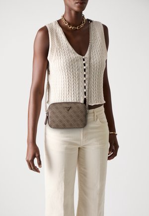 Kobieta ubrana w kremową, bezrękawnikową kamizelkę z grubym splotem, kremowe spodnie z wysokim stanem, złoty łańcuszek oraz brązową, wzorzystą torebkę na ramię.