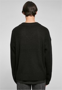 Suéter negro de punto sobredimensionado con textura de canalé y diseño de hombros caídos, que presenta un cuello ancho y un corte relajado.