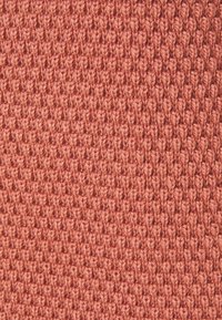 Primer plano de tela de punto rosa que muestra un patrón texturizado de lazos verticales y horizontales interconectados.