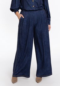 Lange denim broek in donkerblauw met een subtiele geweven textuur, voorzien van zakken en contrasterende beige stiksels.