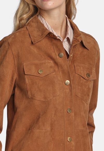 Braune Wildlederjacke mit durchgehendem Knopfverschluss, spitzem Kragen, zwei Brusttaschen und goldfarbenen Beschlägen. Weiche Textur und klassisches Design.