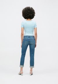 Világoskék, testhez simuló rövid ujjú felső középmosott, egyenes szárú farmernadrággal, amelyen mandzsetták és finom márkajelzés látható a hátsó zsebeknél.