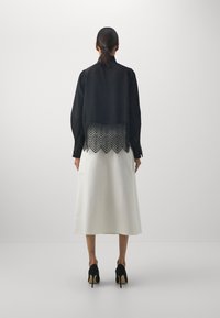 Svart kort blus med spetsdekoration vid fållen, i kombination med en vit midi-kjol och svarta högklackade skor. Slät tygtextur.