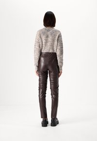 Pantalons en simili cuir marron à taille haute, au design ajusté et à texture côtelée. Portés avec un pull léger et texturé et des chaussures noires.
