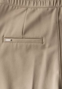 Beige tkanina s hladkým povrchem, která má zadní kapsu. Discretní šití a malá kovová nášivka na kapse dodávají eleganci.