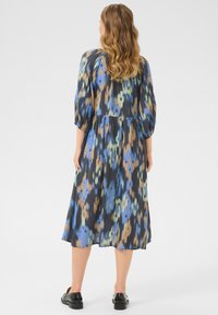 Vestido midi floral en negro con patrones azules, marrones y verdes. Presenta mangas abullonadas, cintura fruncida y una falda fluida. Zapatos negros.