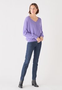 Lavendelfärgad ulltröja med V-ringning, avslappnad passform och långa ärmar, kombinerad med mörk denimjeans och svarta klackiga ankelskor.